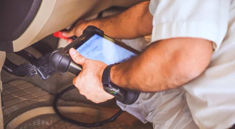 A man is using diagnostic tools to perform a car's electrical repair.