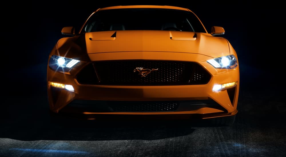 The headlights of an orange 2020 Ford Mustang are lit up in a very dark garage in Cincinnati, OH.