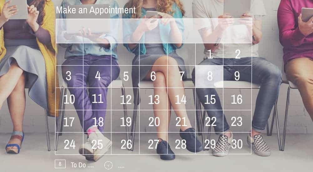 A transparent calendar with the text "Make an appointment" over people in chairs on their devices in a Cincinnati, OH tire shop waiting room