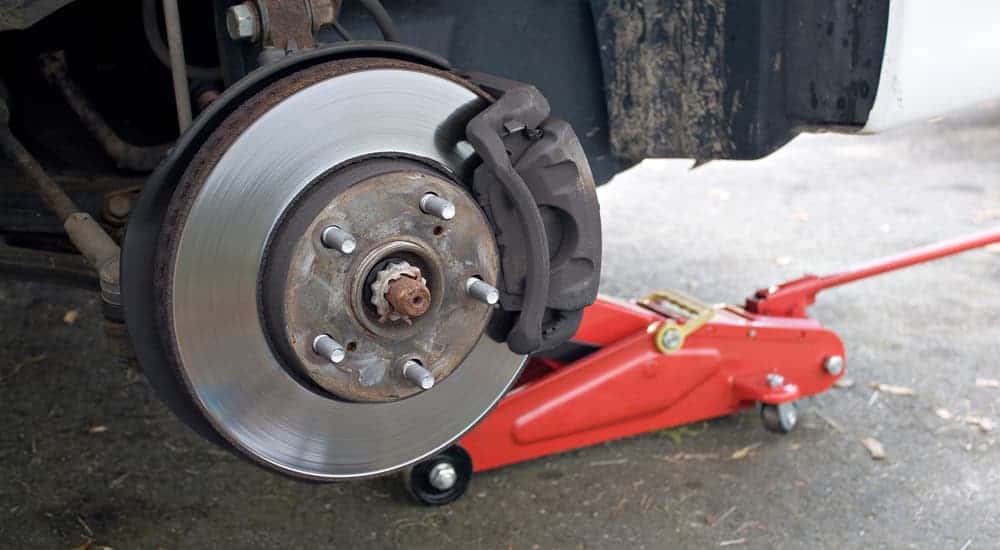 The brake system on a car is shown with a red jack underneath during a brake service at a Cincinnati, OH garage.