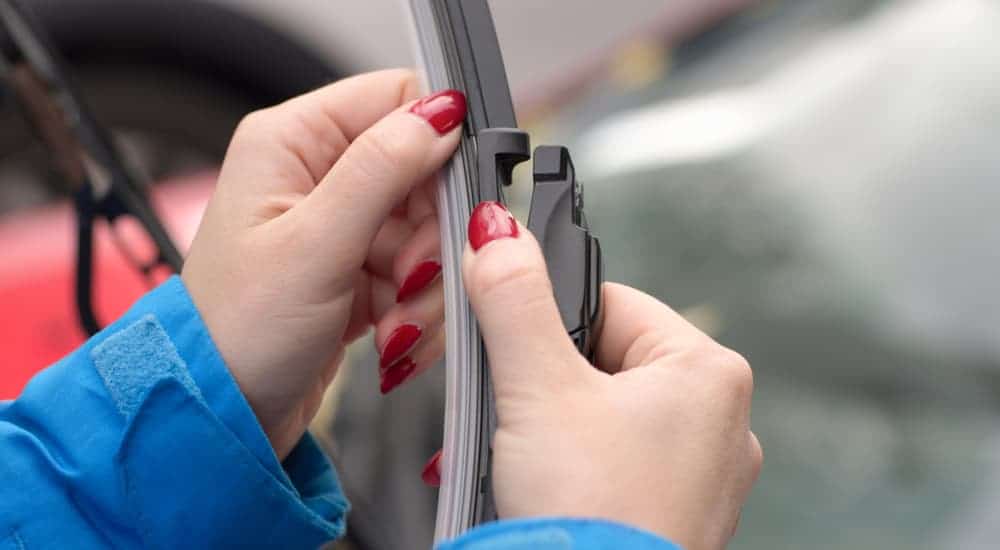 A woman with red painted nails is checking her windshield wiper blades. 