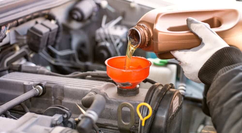 A mechanic is pouring new oil into a car's engine. 