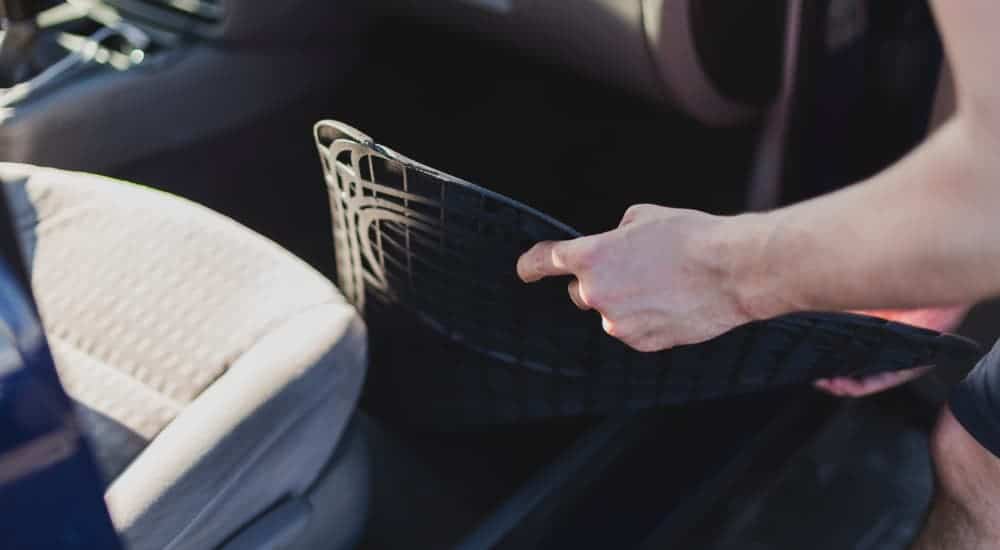 A person is placing rubber floor mats in their car.