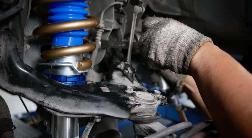 The gloved hands of a Cincinnati mechanic are working on a car's suspension.