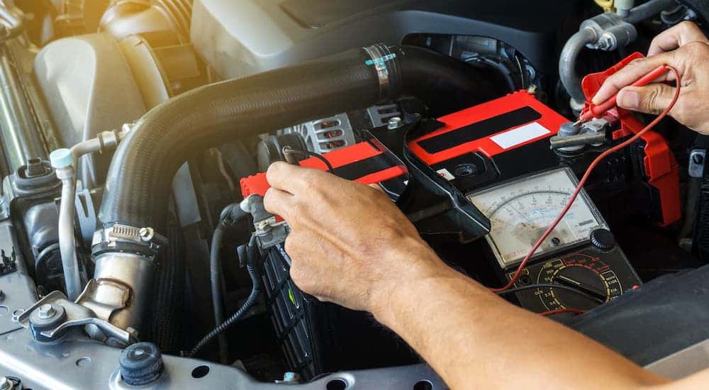 Hands are shown checking the voltage on a car battery at a service shop in Cincinnati.