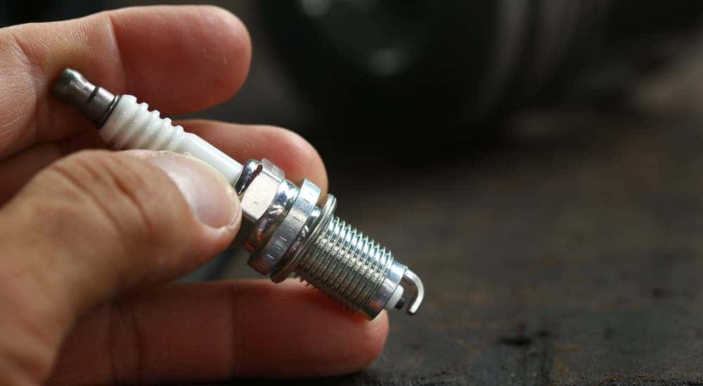 A closeup shows a hand holding a spark plug in a Cincinnati Ford Service shop.