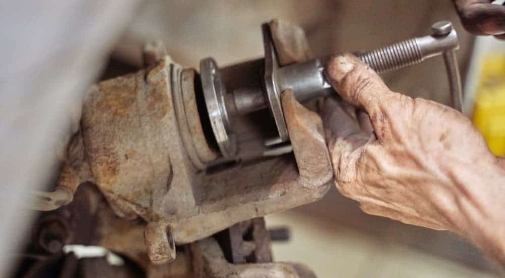 A mechanic is depressing a caliper piston during a brake service.