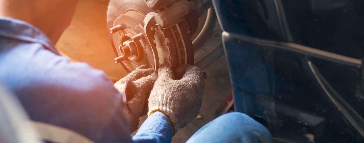 A closeup shows a mechanic working on a car's brakes with gloves.