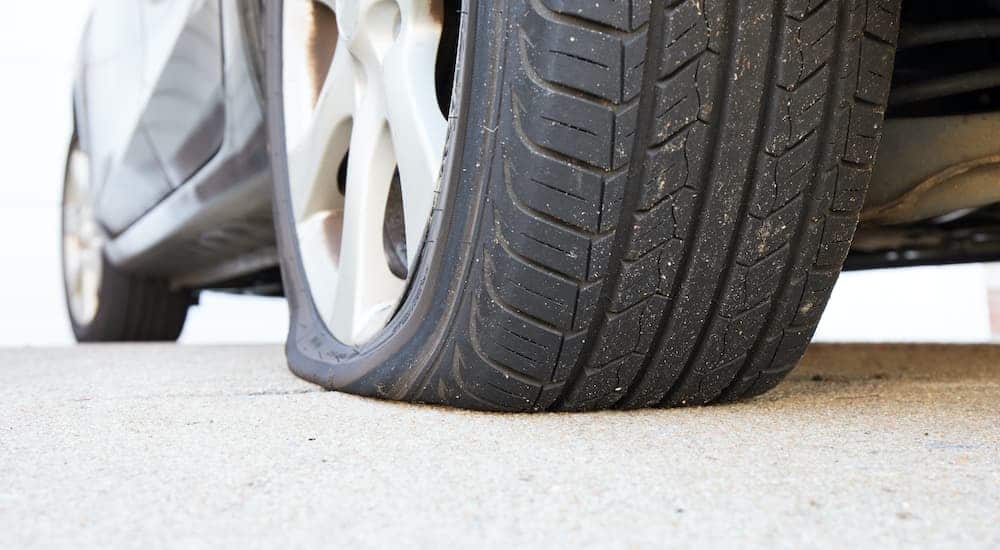 A flat tire is shown on the alloy rim of a grey sedan.