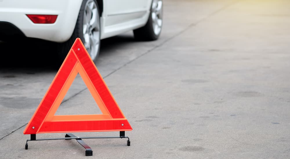 An orange triangle hazard reflector is on the road near a white car.