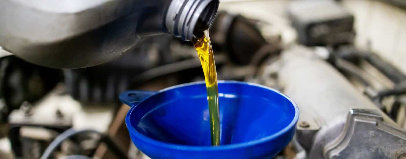A closeup shows oil being poured into a blue funnel.