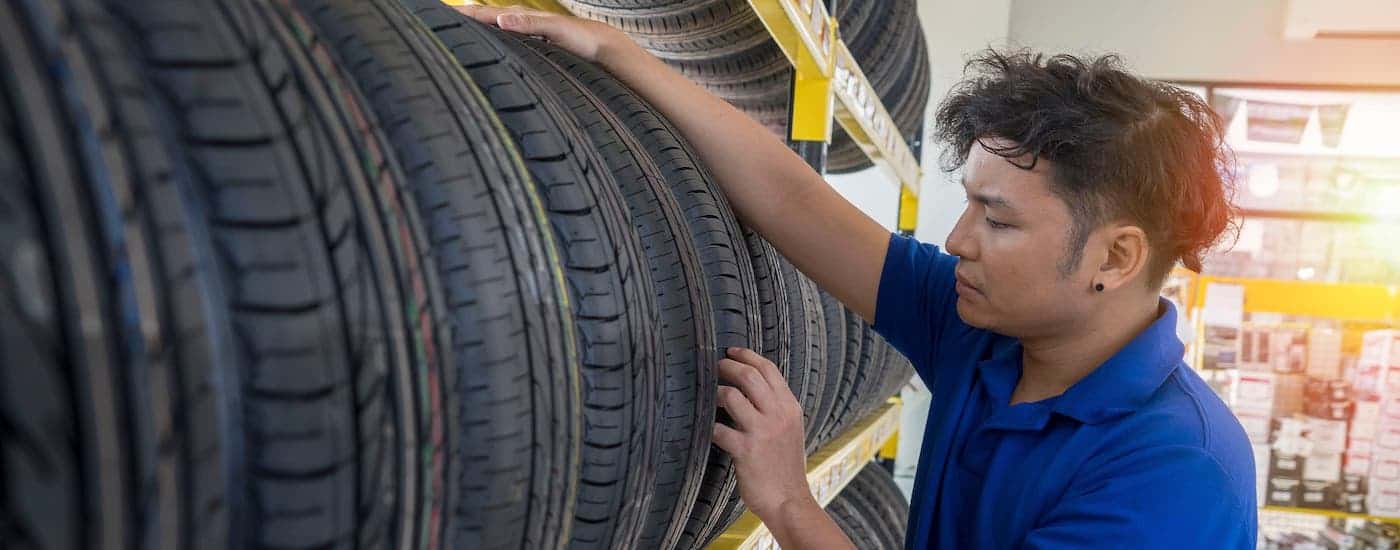 A man in a blue shirt is inspecting a tire on a rack of tires.