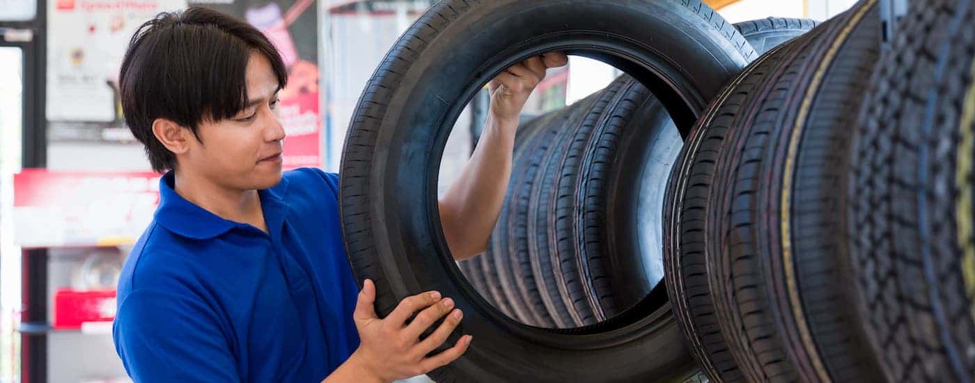 A man in a blue shirt is taking a tire off of a rack of tires.