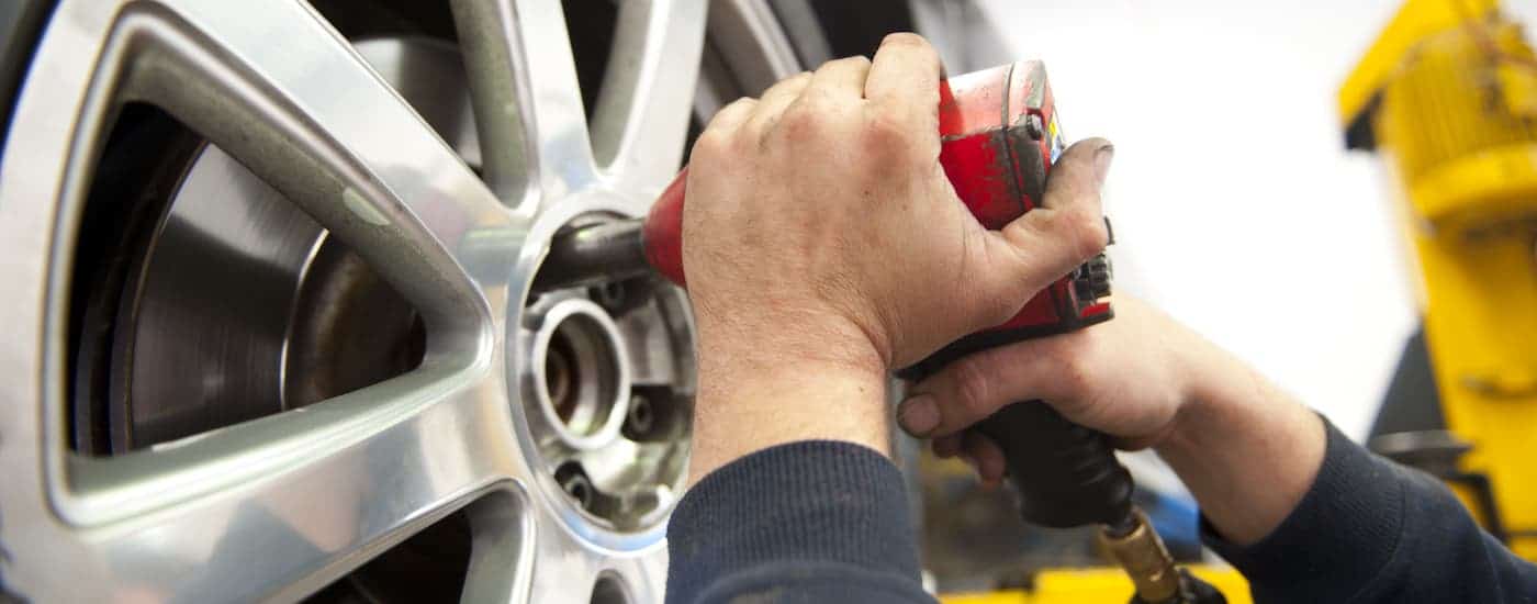 A closeup shows hands using an impact wrench on a car's tire during a Kings Ford service.